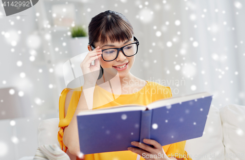 Image of smiling young asian woman reading book at home