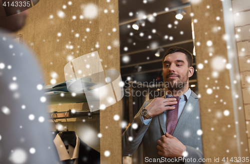 Image of man trying tie on at mirror in clothing store