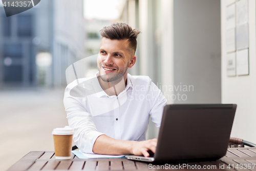 Image of smiling man with laptop and coffee at city cafe