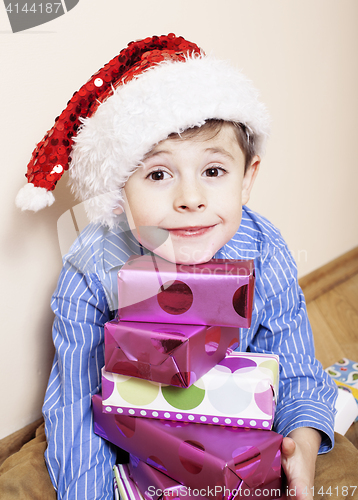 Image of little cute boy with Christmas gifts at home. close up emotional face on boxes in santas red hat