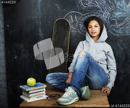 Image of young cute teenage girl in classroom at blackboard seating on ta