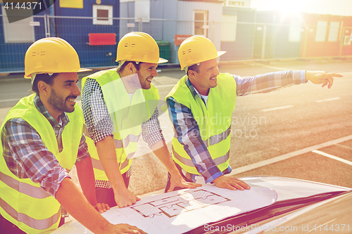 Image of close up of builders with blueprint on car hood