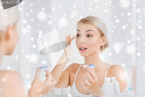 Image of young woman putting on contact lenses at bathroom