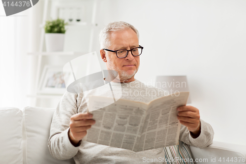 Image of senior man in glasses reading newspaper at home