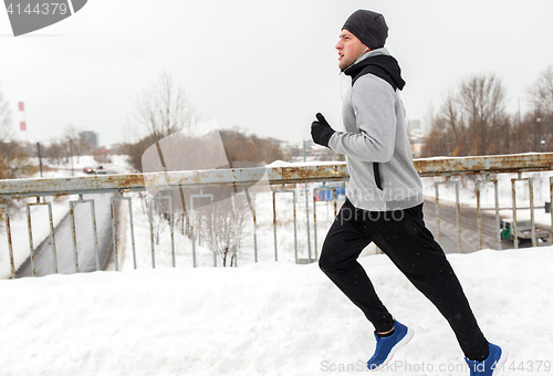 Image of man in earphones running along winter bridge