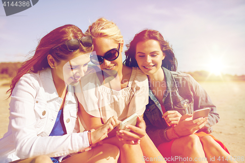 Image of group of happy women with smartphones on beach