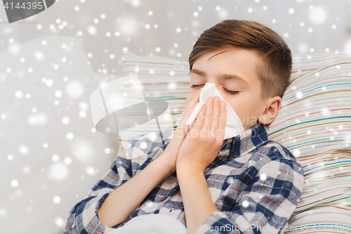 Image of ill boy lying in bed and blowing his nose at home