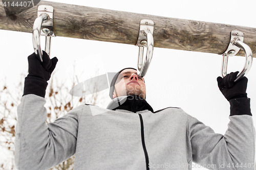 Image of young man exercising on horizontal bar in winter