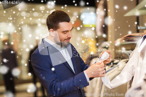 Image of happy young man choosing clothes in clothing store