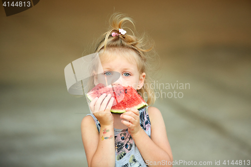 Image of Adorable blonde girl eats a slice of watermelon outdoors.