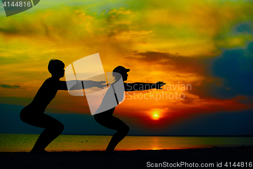 Image of Yoga people training and meditating in warrior pose outside by beach at sunrise or sunset.