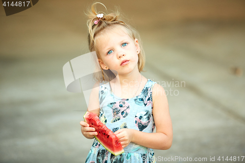 Image of Adorable blonde girl eats a slice of watermelon outdoors.