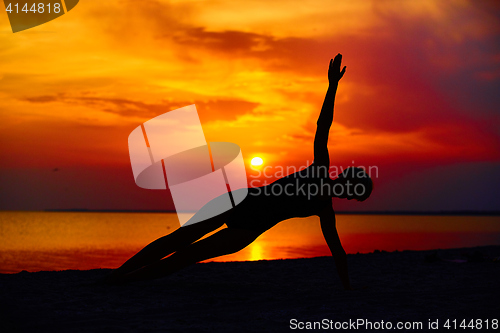 Image of Silhouette of woman standing at yoga pose on the beach during an amazing sunset