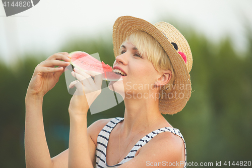 Image of Beautiful girl in straw hat eating fresh watermelon. Film camera style