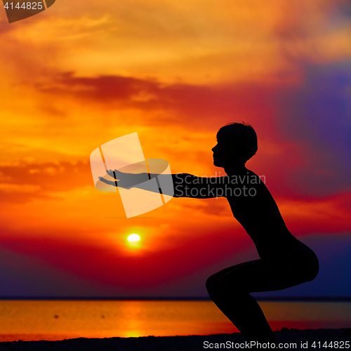 Image of Silhouette of woman standing at yoga pose on the beach during an amazing sunset