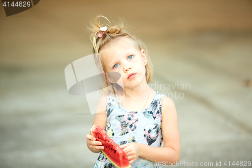 Image of Adorable blonde girl eats a slice of watermelon outdoors.