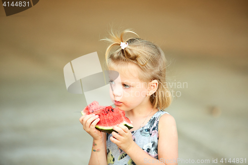 Image of Adorable blonde girl eats a slice of watermelon outdoors.