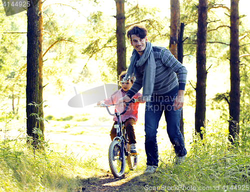 Image of father learning his son to ride on bicycle outside, real happy f