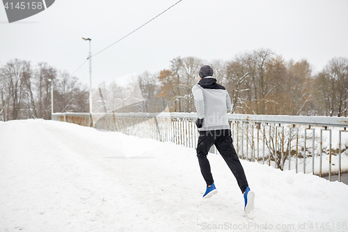 Image of man running along snow covered winter bridge road