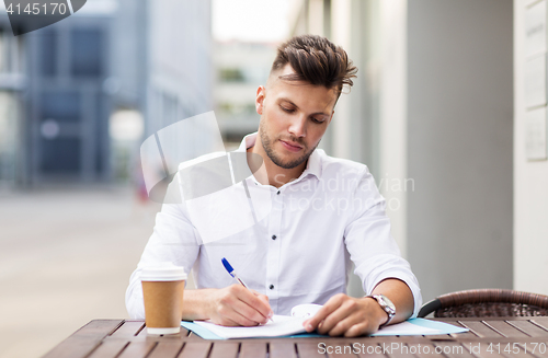 Image of man with coffee and folder writing at city cafe