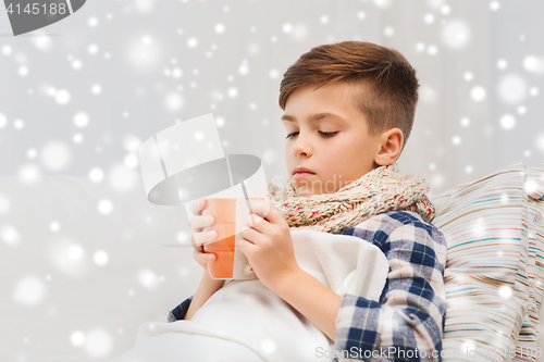 Image of ill boy with flu in scarf drinking tea at home