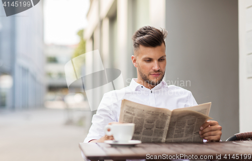 Image of smiling man reading newspaper at city street cafe