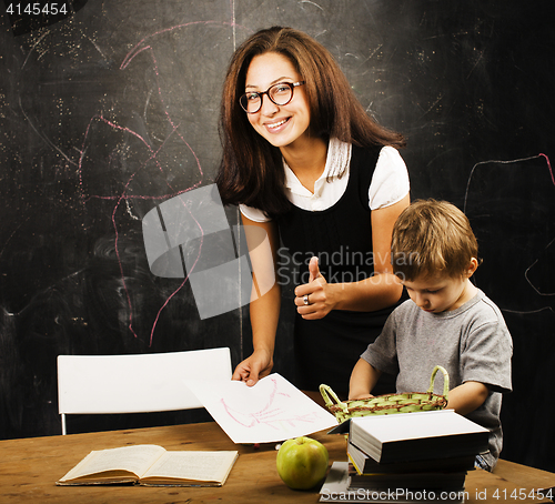 Image of little cute boy with young teacher in classroom studying at blackboard, lifestyle education people concept
