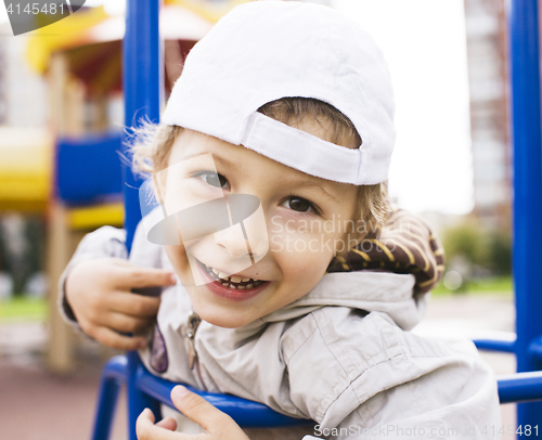 Image of little cute real boy playing on playground, hanging on gymnastic ring cheerful