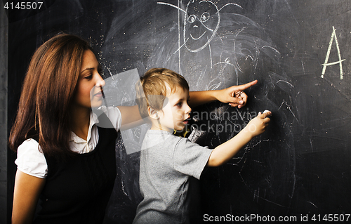 Image of little cute boy with young teacher in classroom studying at blackboard, lifestyle education people concept