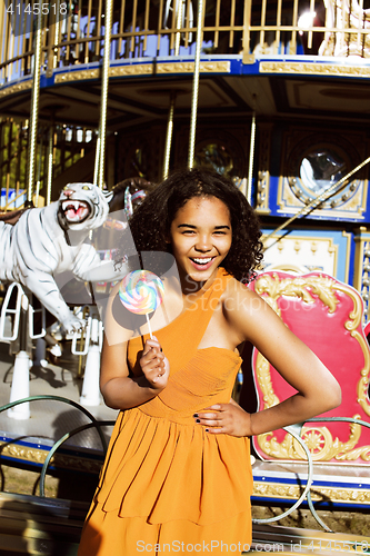 Image of cool real teenage girl with candy near carousels at amusement pa