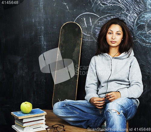 Image of young cute teenage girl in classroom at blackboard seating on ta