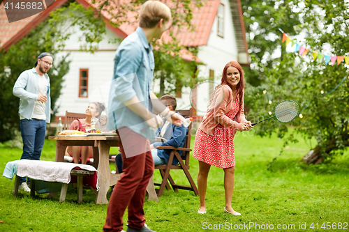 Image of happy friends playing badminton at summer garden