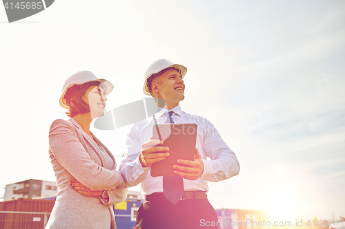 Image of happy builders in hardhats with tablet pc outdoors