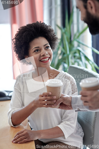 Image of happy woman taking coffee from man in office