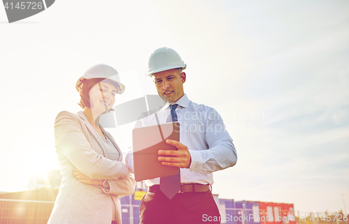 Image of happy builders in hardhats with tablet pc outdoors