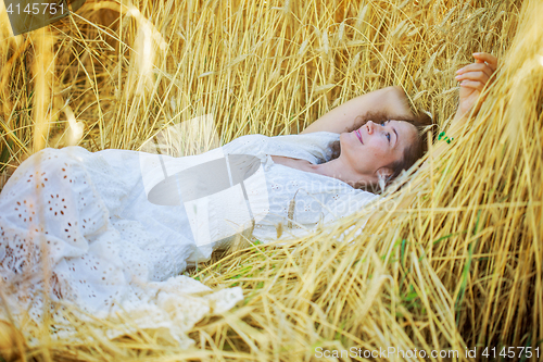 Image of smiling woman in white dress lying among the ears of wheat