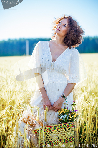 Image of beautiful smiling woman in a white dress standing among the ears