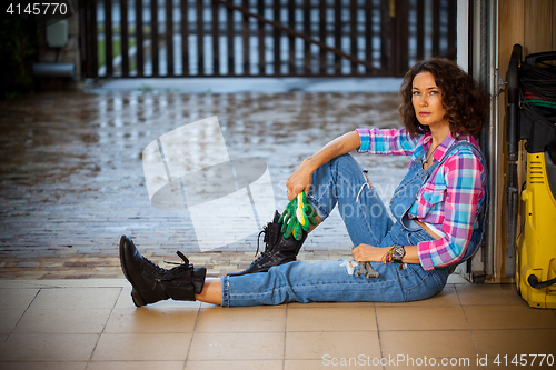 Image of beautiful woman in blue overalls mechanic sitting on the thresho