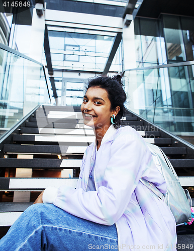 Image of young cute modern indian girl at university building sitting on stairs reading a book, wearing hipster glasses, lifestyle people concept