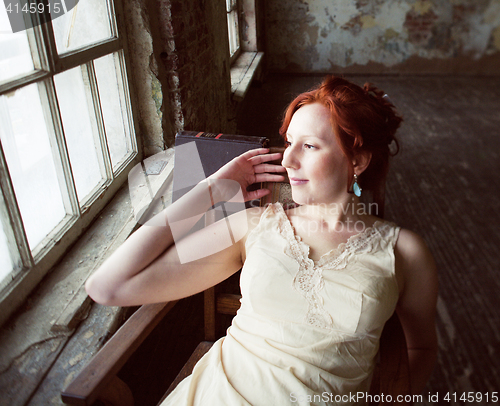 Image of pretty young red hair woman in old -fashioned style room sitting smiling at window and typing machine, art vintage concept