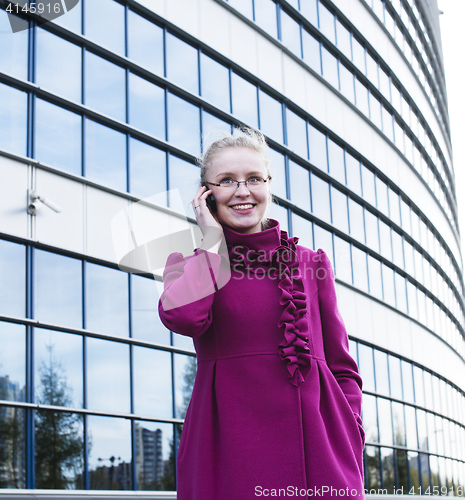 Image of portrait of pretty young business woman in glasses talking on phone near modern building, lifestyle people concept