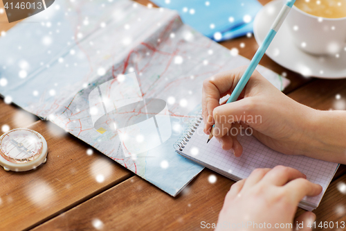 Image of hands with map and compass writing to notebook