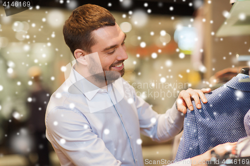 Image of happy young man choosing clothes in clothing store