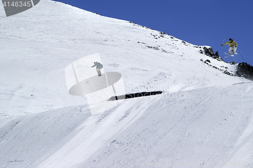 Image of Snowboarder and skier jumping in snow park at ski resort on sunn