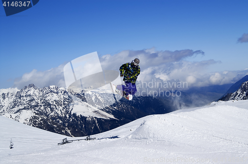 Image of Snowboarder jumping in terrain park at snow mountain on sunny wi