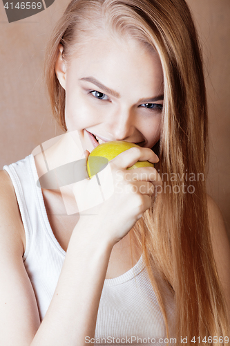 Image of young pretty blond woman with green apple happy cheerful smiling close up on warm brown background, lifestyle people concept