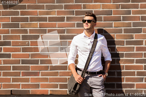 Image of young man in sunglasses with bag over brickwall