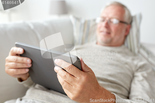 Image of senior man with tablet pc lying on sofa at home