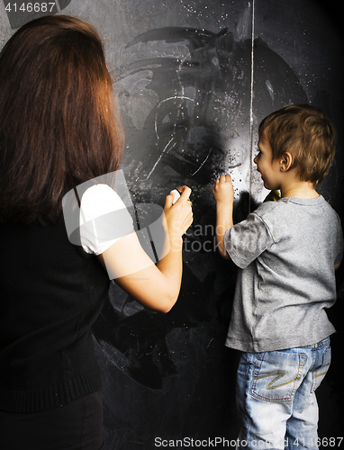 Image of little cute boy with young teacher in classroom studying at blac