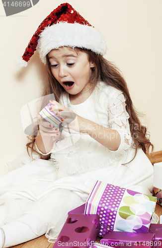 Image of little cute girl in santas red hat waiting for Christmas gifts. smiling adorable kid. White new dress home interior 